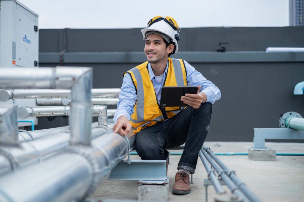 An HVAC worker on the job wearing a hard hat and safety vest.