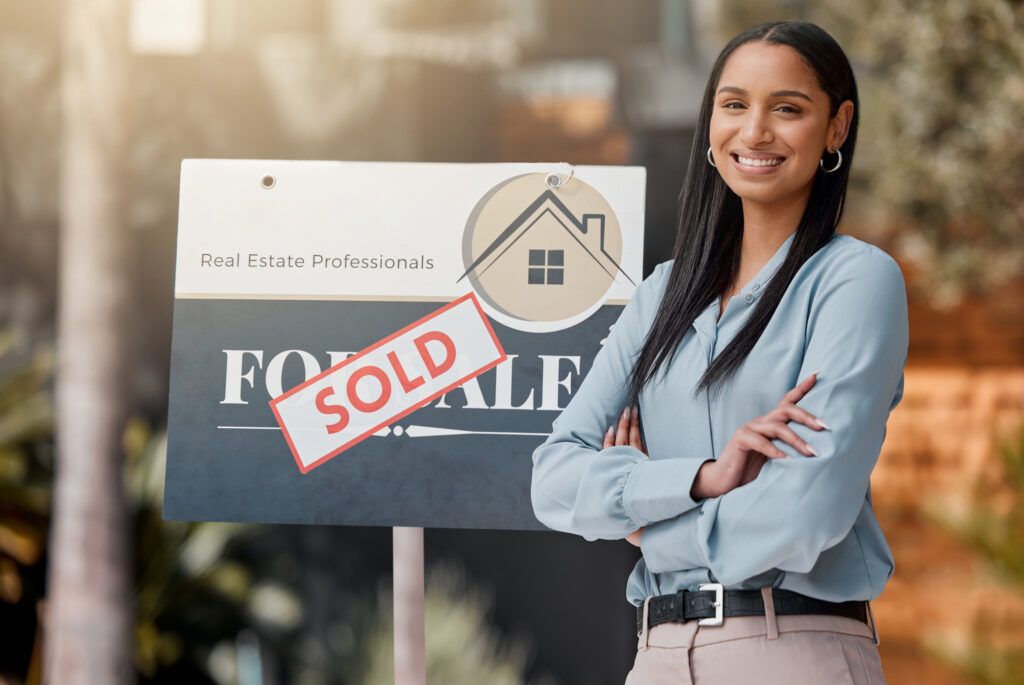 A real estate agent happily stands outside in front of her sold sign.