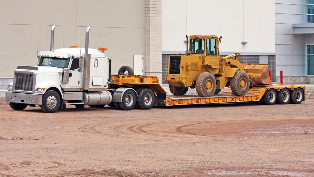 A semi truck hauls a construction vehicle to a home builders’ worksite.