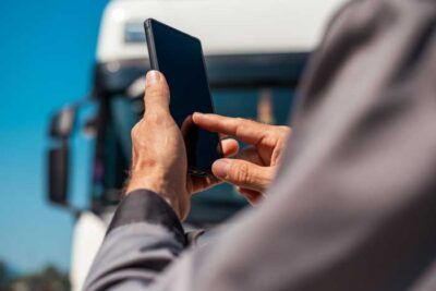 A fleet driver stands outside his truck entering his PIN on his mobile phone.