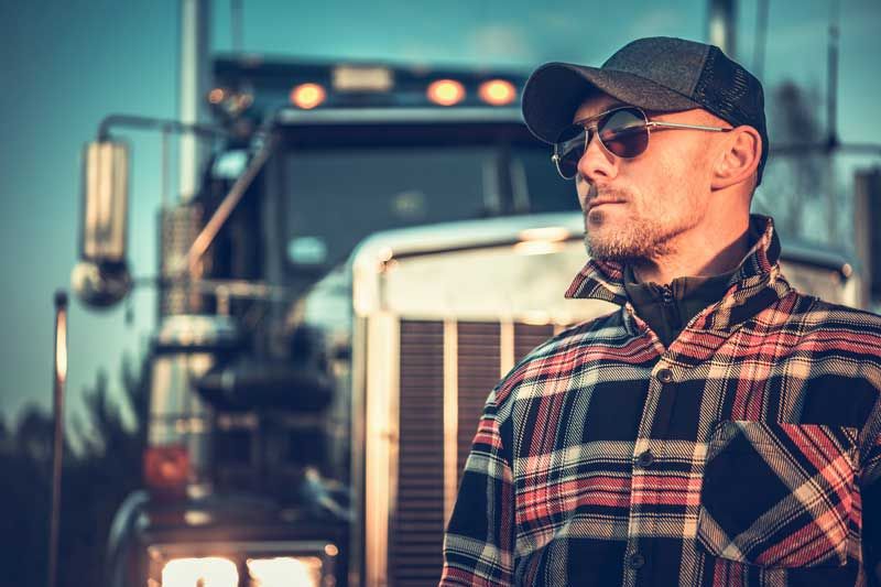 A proud truck driver stands outside his semi truck.